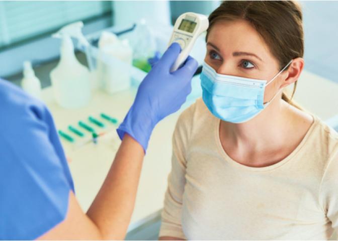 A healthcare worker takes the temperature of a female patient wearing a mask