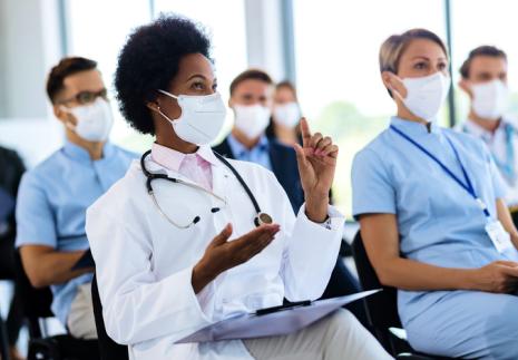 Woman raising hand in a group of healthcare workers seated in classroom setting wearing masks